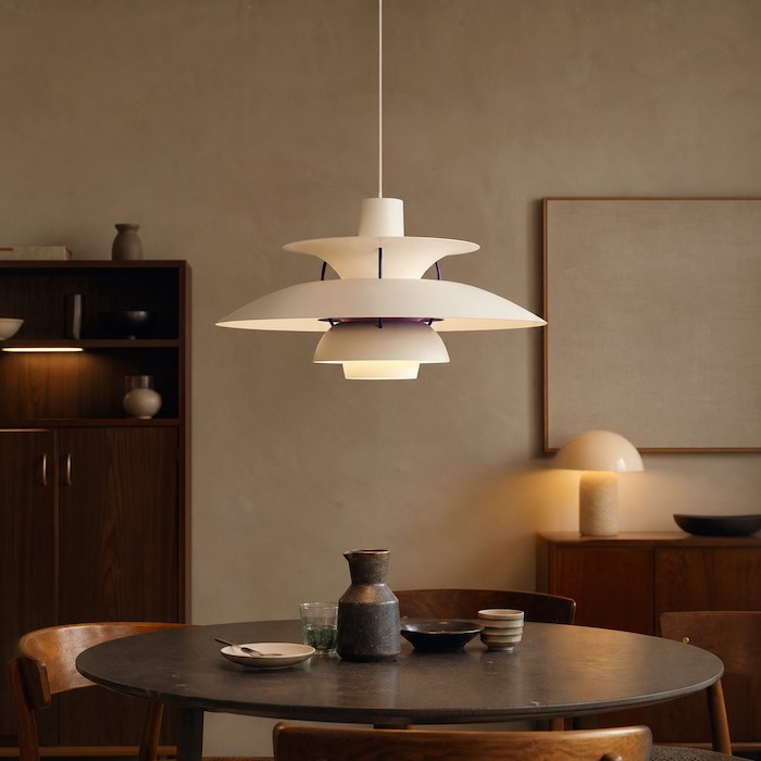 Retromodernes Esszimmer mit mehrschichtiger Metallpendelleuchte, Vintage-Holzstühlen und ruhigen, matten Wänden.