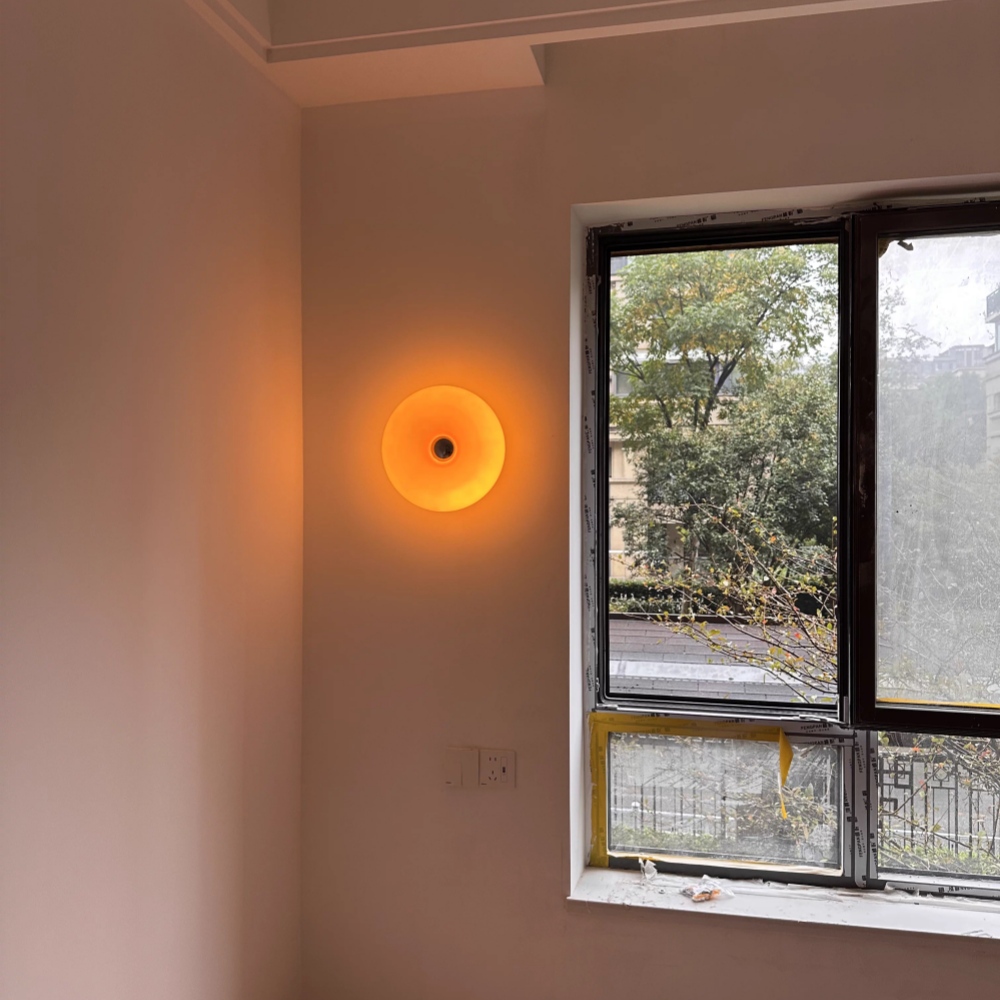 Kundenfoto der orangefarbenen Donut-Wandleuchte neben einem Fenster