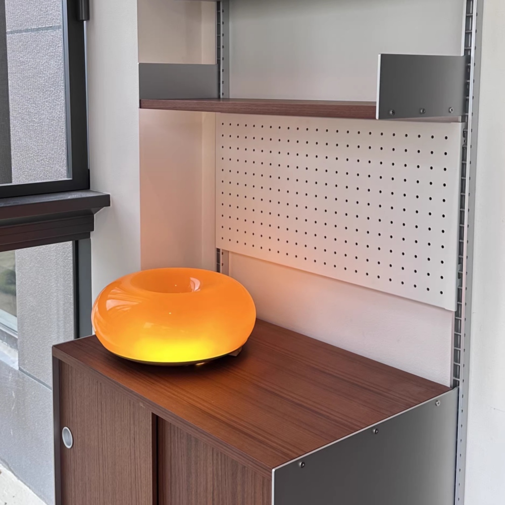 Kundenfoto der orangefarbenen Halorentis Tischleuchte auf einem Schrank