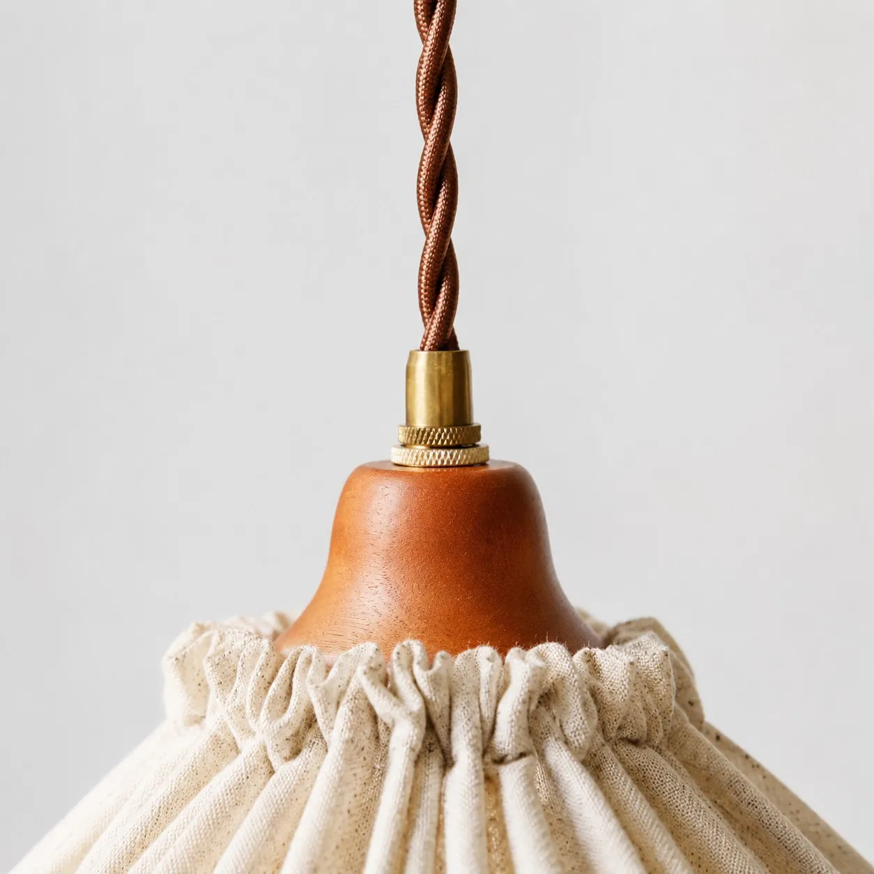 Close-up of twisted brown cord, brass fitting and warm wood socket cover
